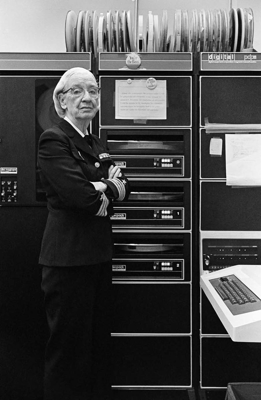 Black and white photograph of a woman with glasses wearing a US Navy suit, standing next to a computer.