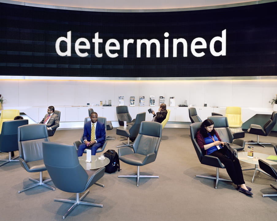 Photo of a lounge with people in comfortable chairs, the word ‘determined’ on a large screen in the back