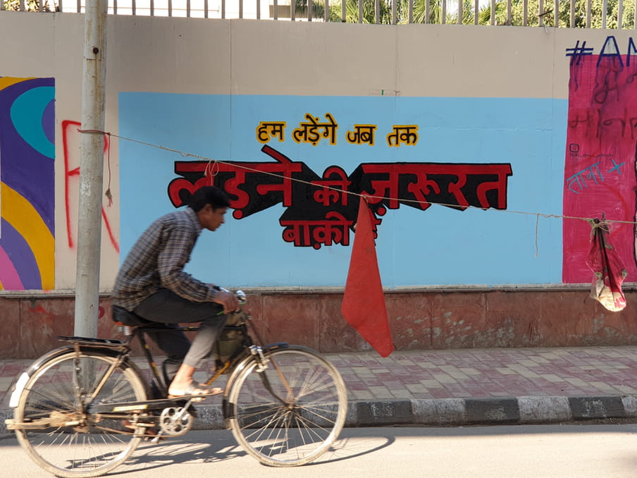 A cyclist pedals past a wall graffiti in Hindi that says "We will fight till there is reason left to fight" near Jamia Millia University.
