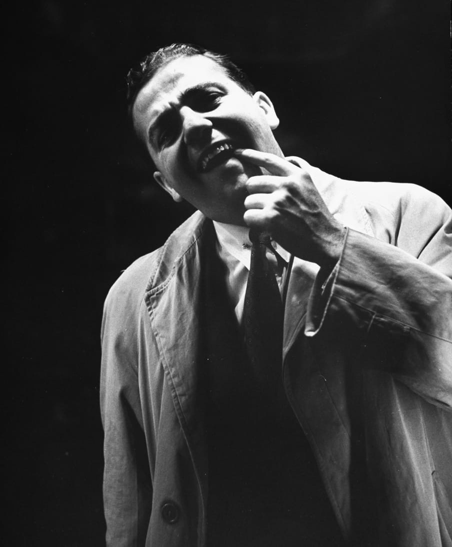 Old black and white photo of a man checking his teeth in a mirror, photographed from the back of the mirror. 