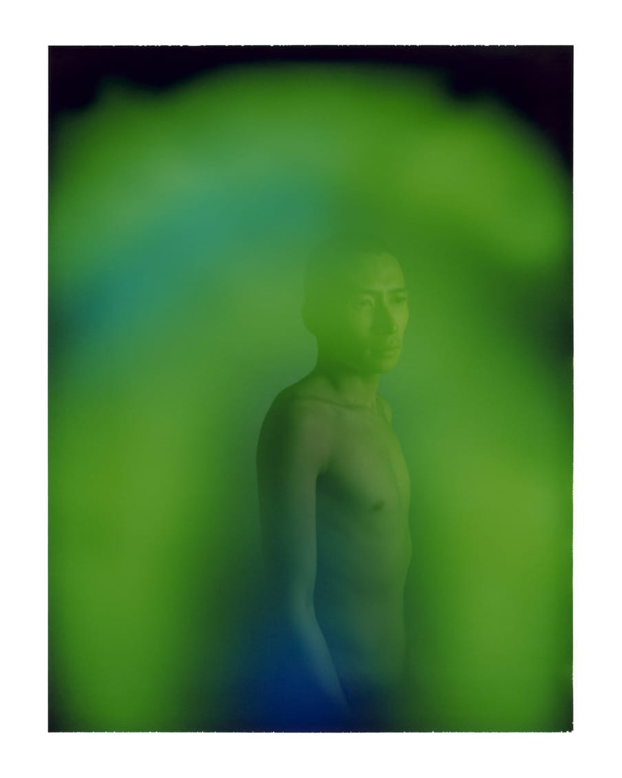 Portrait of a man with dark, short hair and no shirt on. A green glow covers the image.