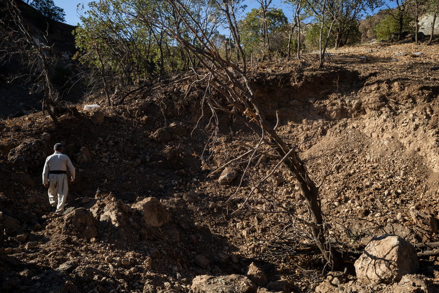 Photograph of a man’s back as he walks on a brown patch of earth strewn with small and big rocks