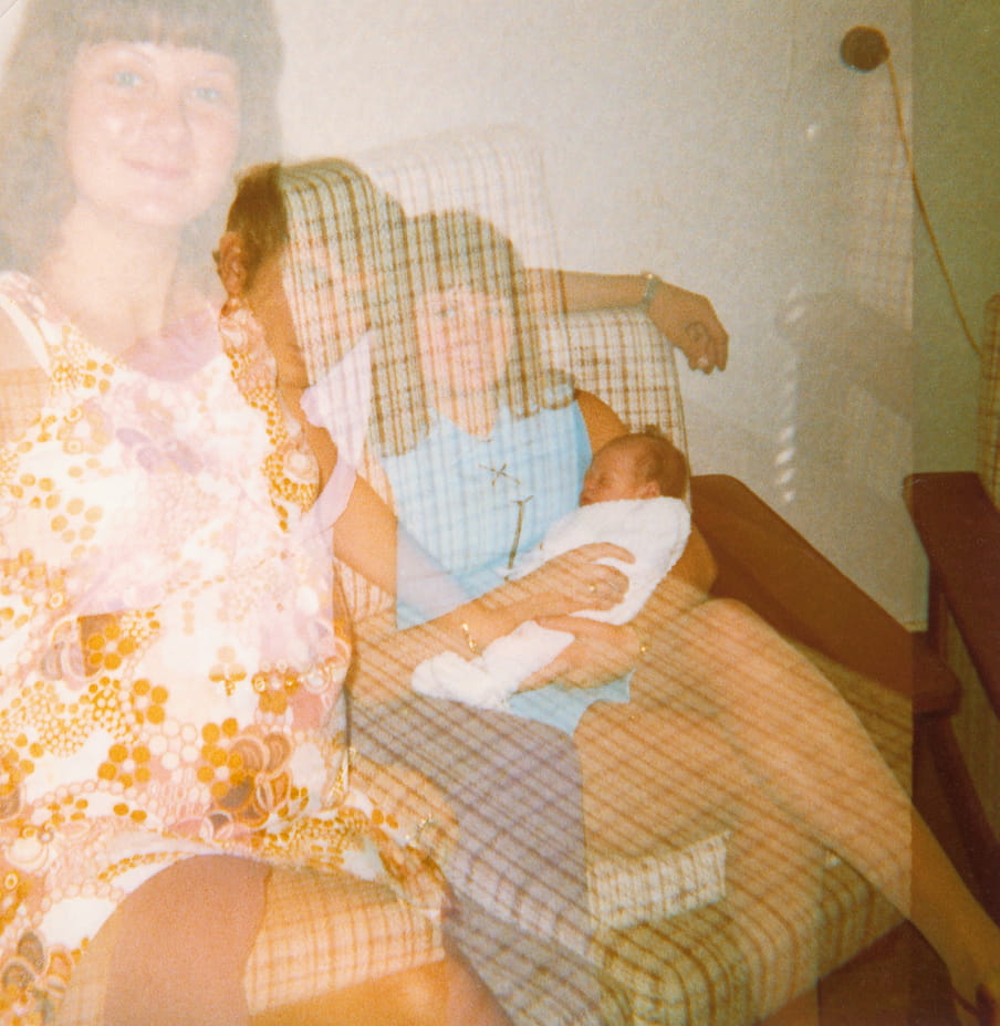 A couch with two women sitting on it - one holding a baby - and a man in the middle. Due to a double exposure on the film the people on the picture are see through.