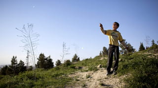 A boy in a yellow jumper flying a kite - on a hill with blue sky in the background