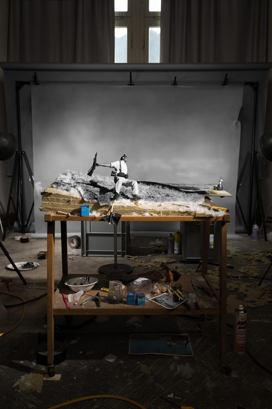 Diaromas of a soldier with a gun in his hand, falling on his back, in a photo studio, with props laying around.
