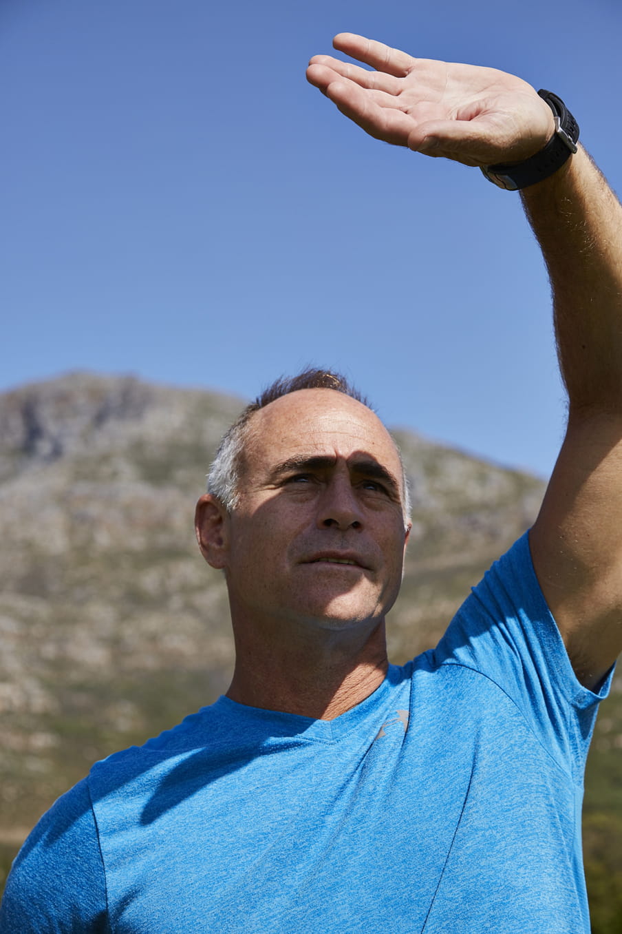 Photo of a man in a blue shirt looking up, blocking his eyes from the sun with his arm