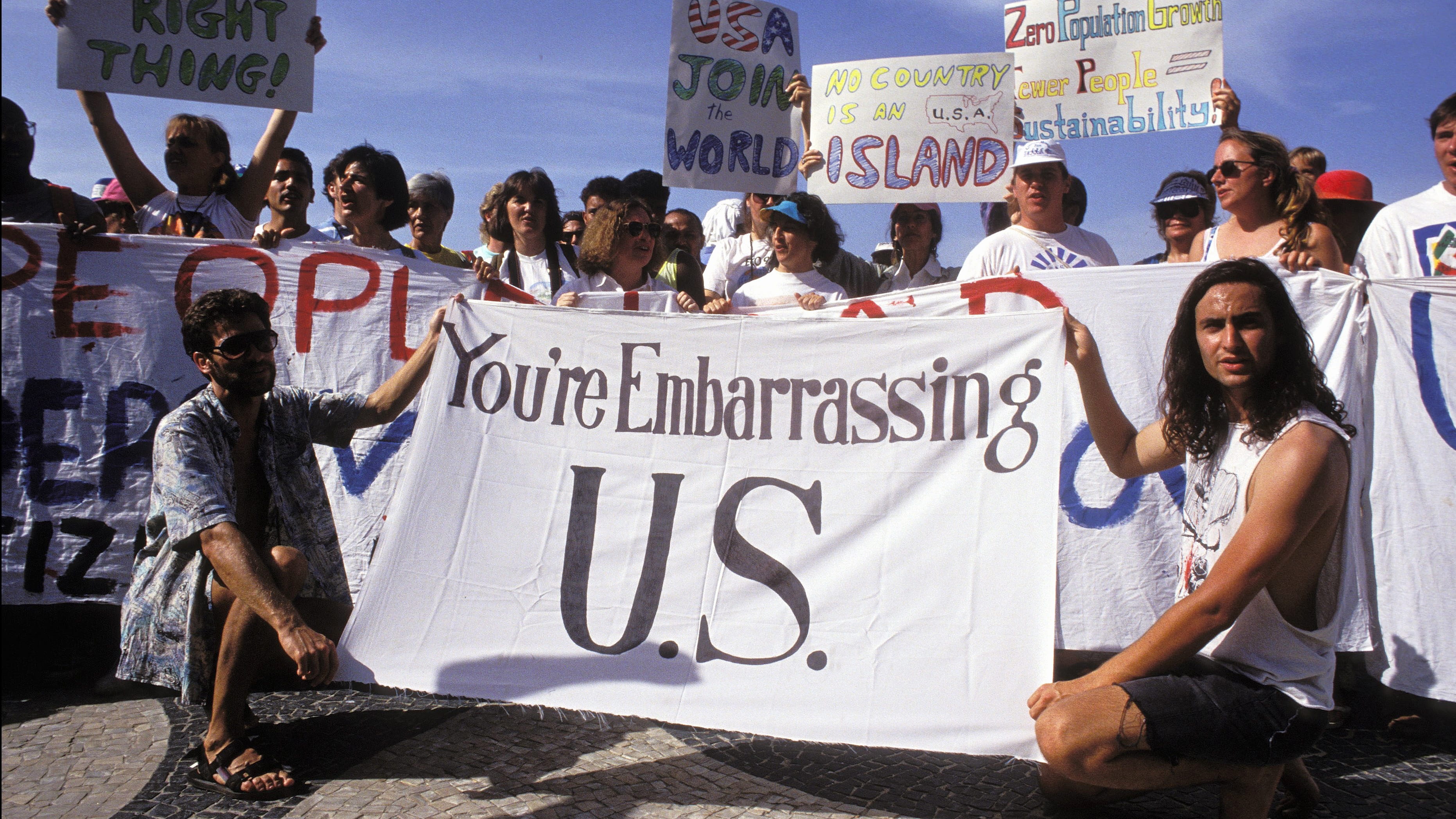 Old photo of people protesting with signs, the biggest one stating ‘You’re Embarrassing U.S.’