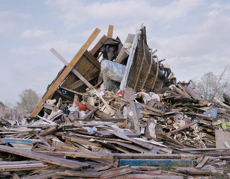 Photo of a pile of rubbish where a house use to be, personal items like a mattress and a childs toy sticking out