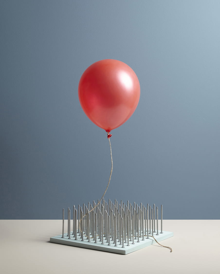 Colour photograph of a red ballon floating over a bed of nails.