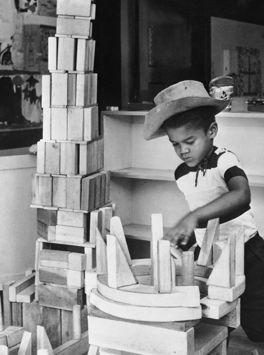 Old black and white photo of a boy with a cowboy hat building a tower of blocks 