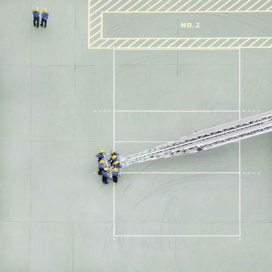 Photograph taken from above on a mint green court showing a group of firemen around a nacelle.