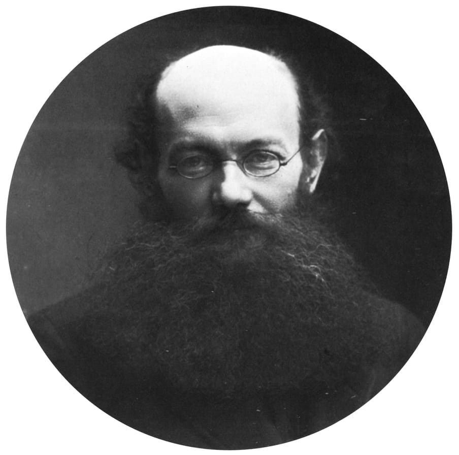 Black and white archival photographic portrait of a bolding man with a beard and glasses. 