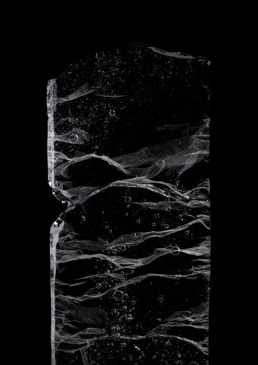 Photo of a block of ice against a black background, showing some bubbles and lines in it, all in different sizes
