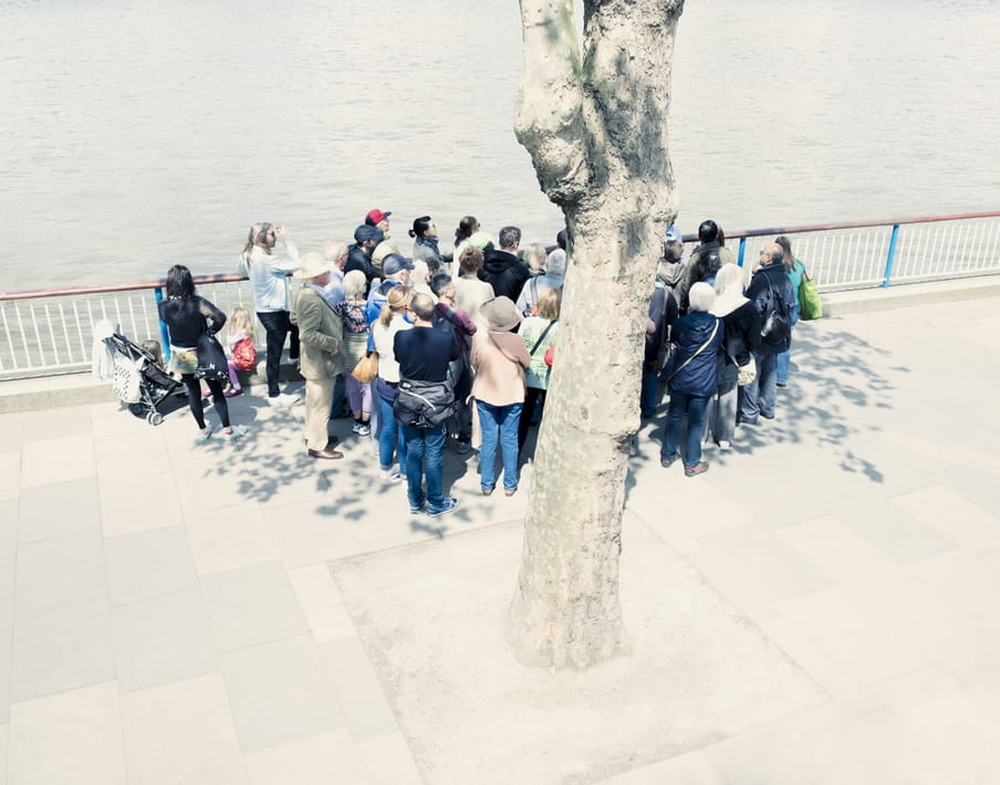 Group of people standing close together on a boulevard overlooking water