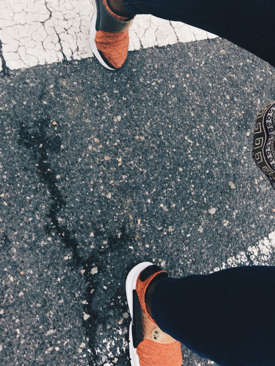 Feet in orange running shoes walking on a zebra crossing.