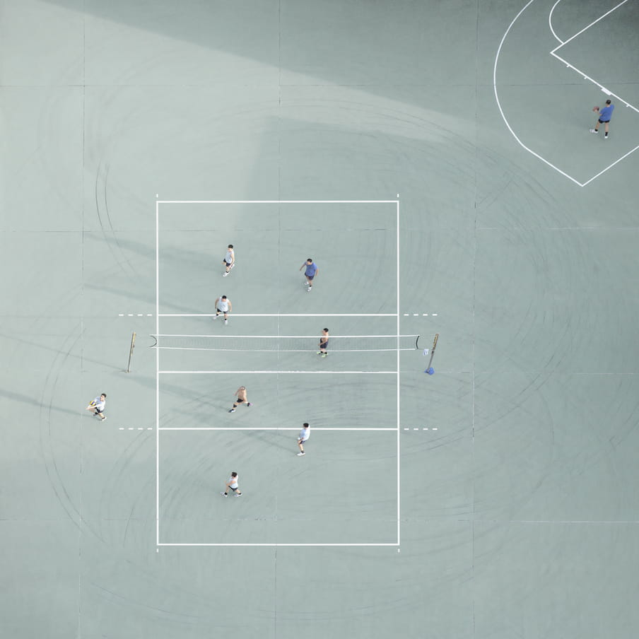 Photograph taken from above of men playing volleyball on a mint green court.