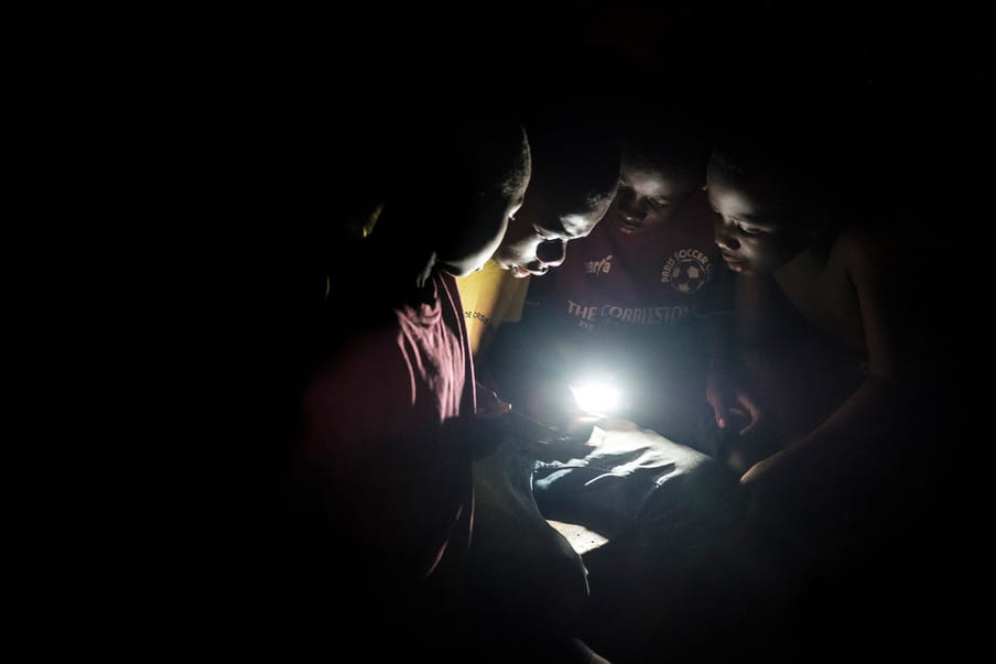 Four children are gathered around a luminous element, hold by a boy with a yellow top. They all look in the direction of the light.