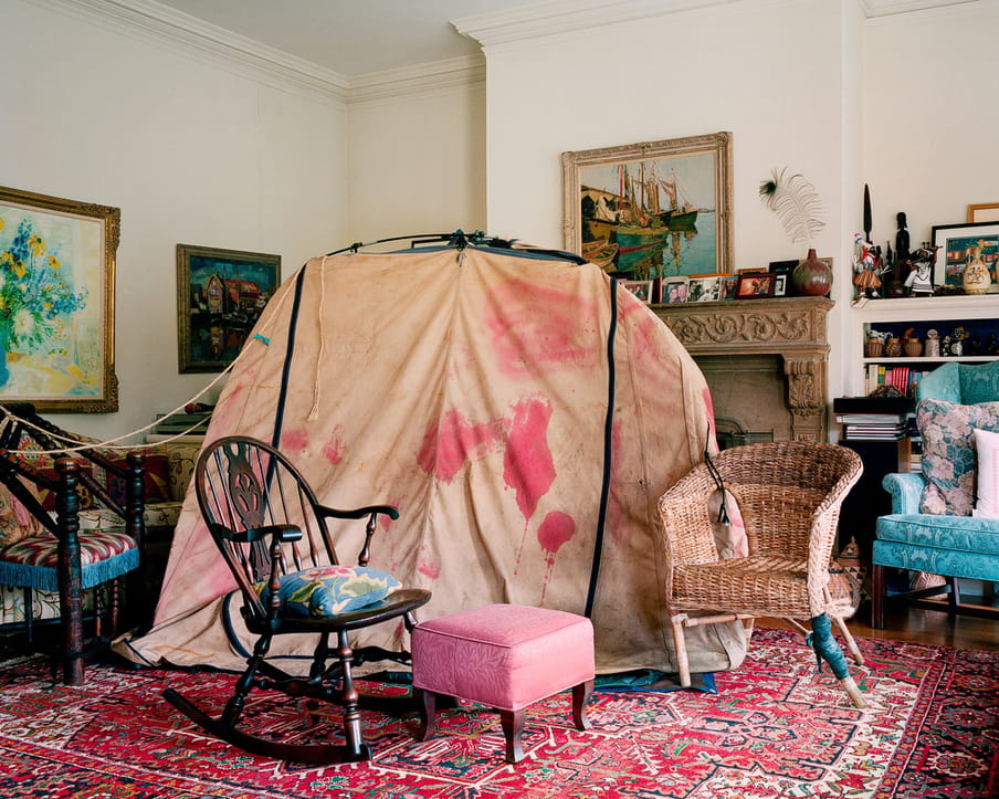 Photo of a living room of a middle or upper class house, with homeless shelter in it made up from different pieces of cloth and an old tent