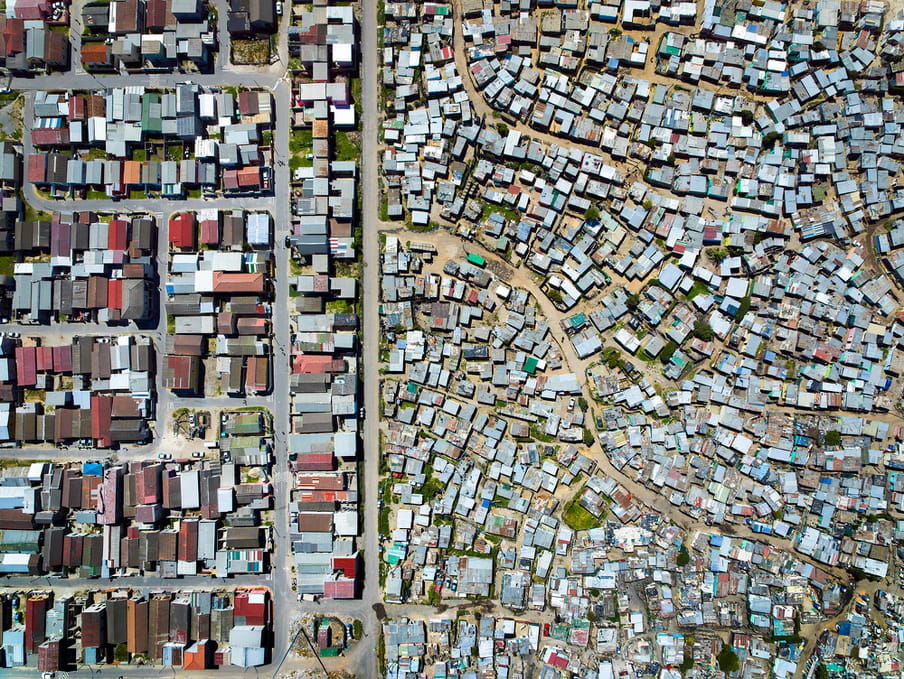 Drone photo of a land. On the left a shanty town, on the right a residential aerea. 
