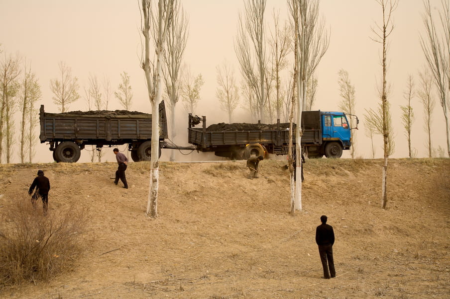 Photograph showing the wheel of blue truck in fire. A few man are standing near by.