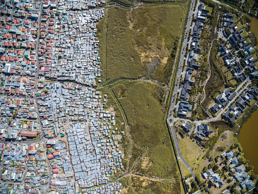 Drone photo of a land. On the left a shanty town, on the right a residential aerea. 