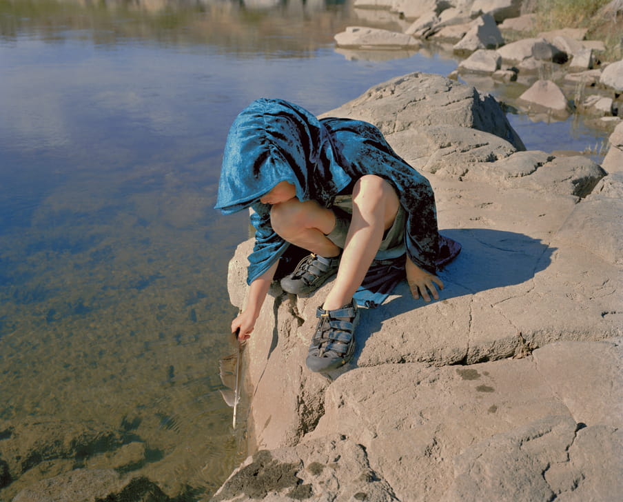 Photo of a boy playing with a feather at a river side