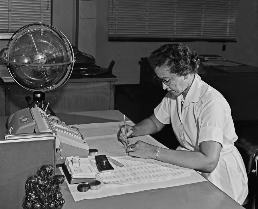 Black and white photograph of a woman with glasses sitting at a desk, working.