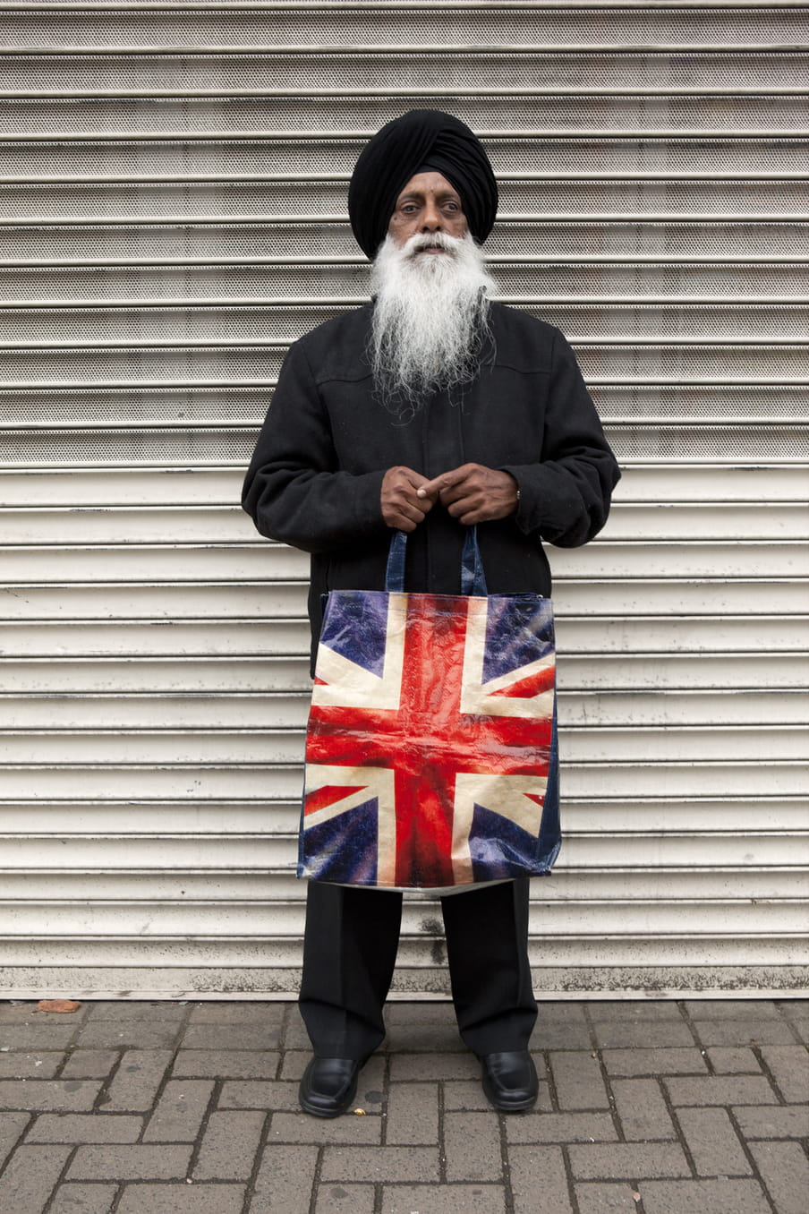 Photo of a Sikh man standing with a bag in his hands, showing the UK flag