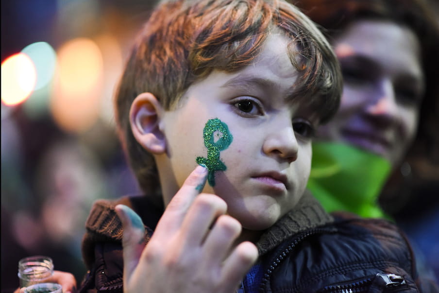 Photo of a young boy at a rally with a green venus symbol on his face made of glitter