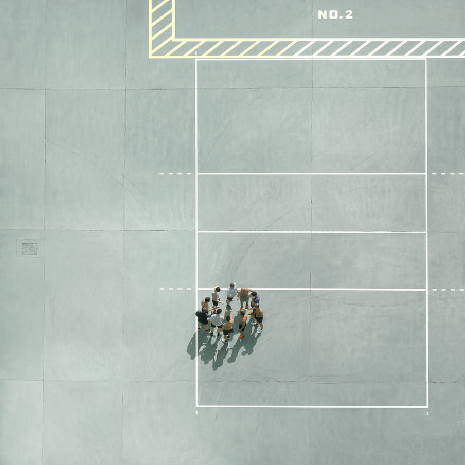 Photograph taken from above on a mint green court showing a group of men gathered in a circle.