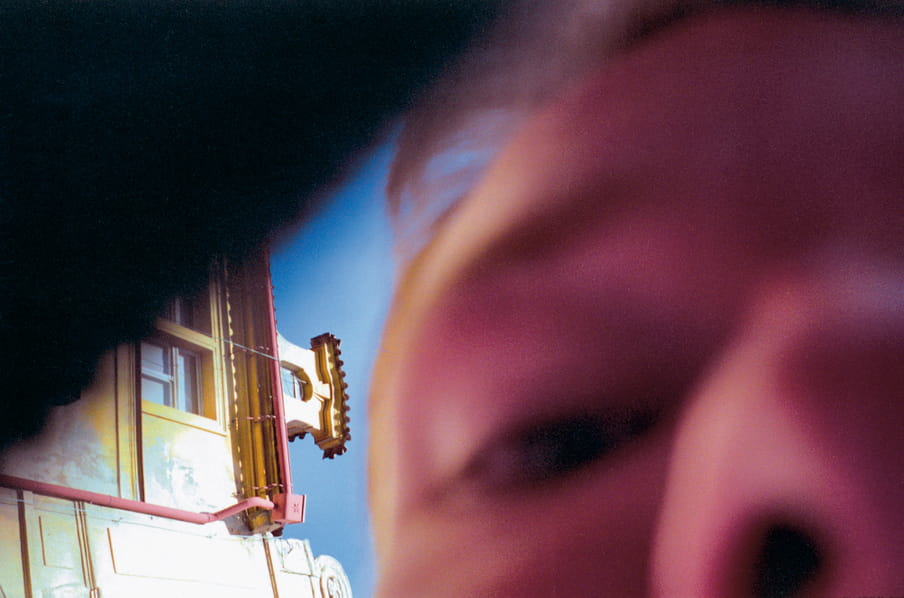 A close up photo of the nose and eye of a man, out of focus, outside with a building in the background.