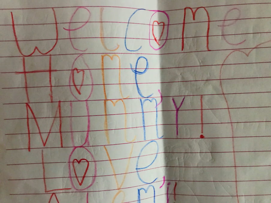 A colourful crayon message on lined paper that reads "welcome home, mummy!"