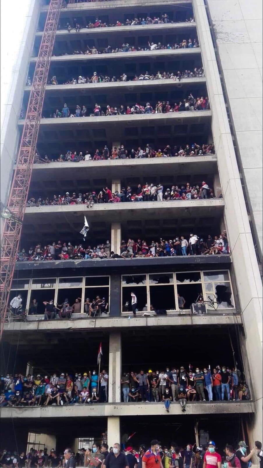 Protestors in Iraq objecting to deteriorating living conditions and corruption. A nine story building filled with people protesting.