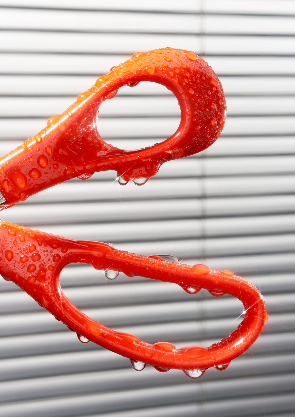 Close up photograph of a pair of bright orange scissors covered with drops of water.