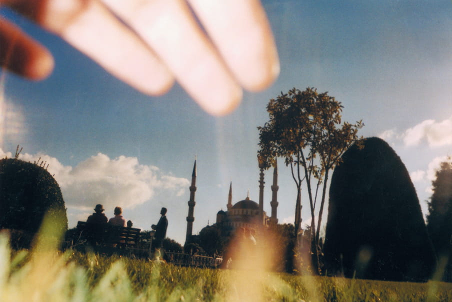 Photo of a building. At the top of the image a hand is blocking the photograph, at the bottom grass.