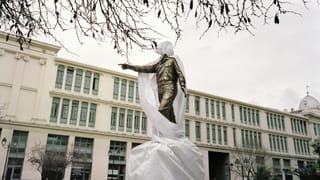 A half-covered statue being restored in Athens in front of a government building. 