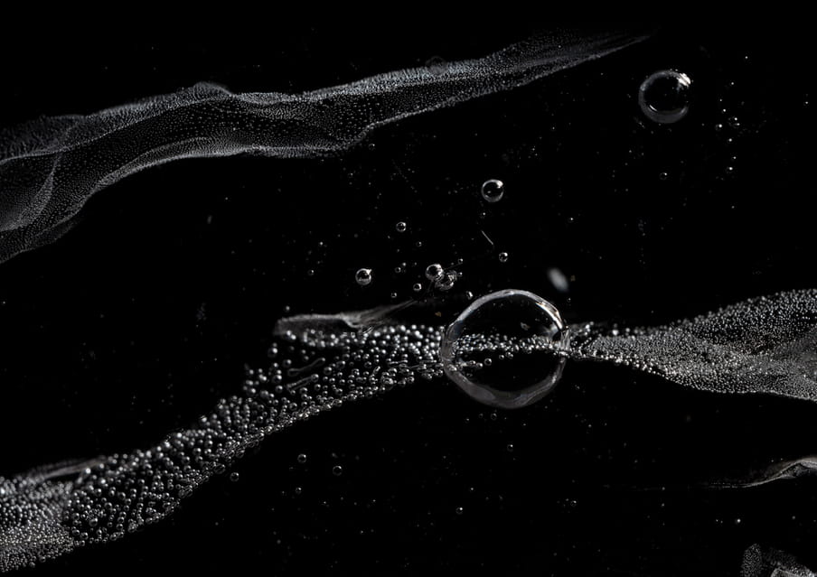 Close up photo of a block of ice against a black background, showing bubbles of different sizes in it, and one big one around the middle