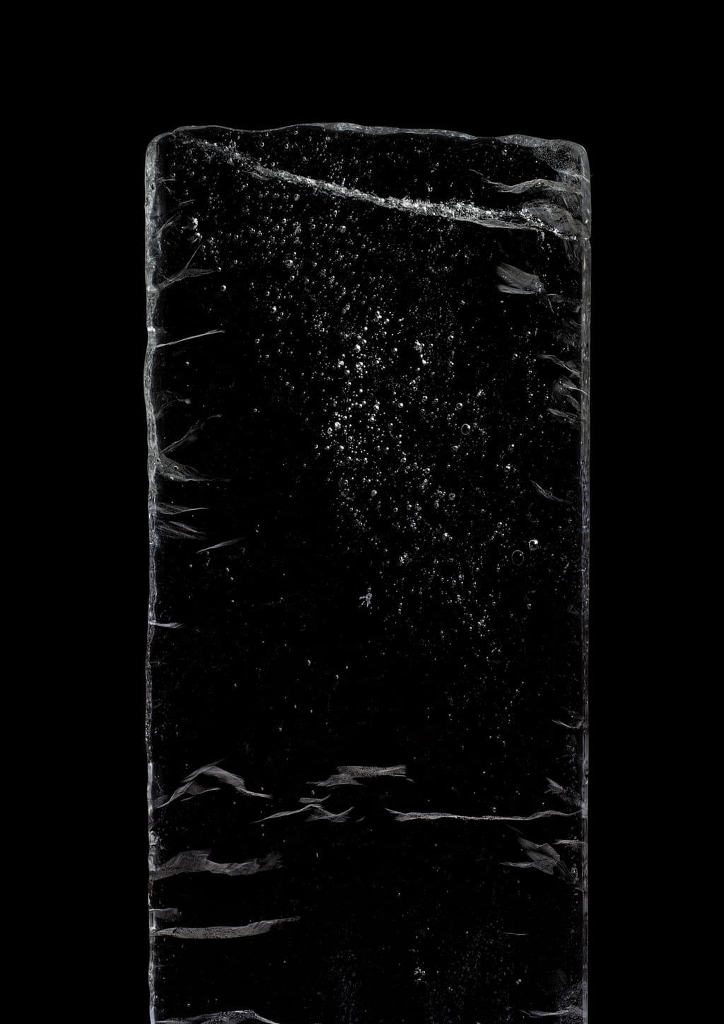 Photo of a block of ice against a black background, showing a small amount of bubbles in it with different sizes.