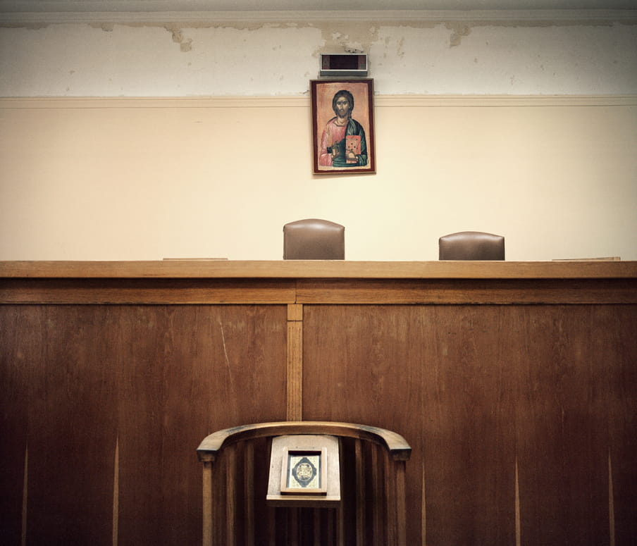 A stand before an empty courtroom, which badly needs a coat of paint, with an artistic religious portrait  on the wall. 