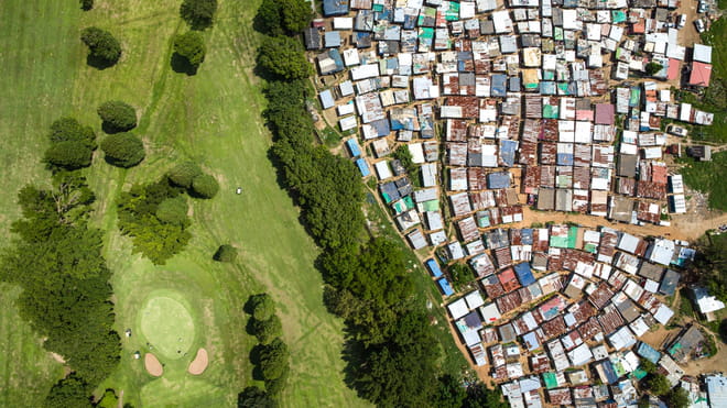 Drone photo of a land. On the right a shanty town, on the left a residential aerea. 