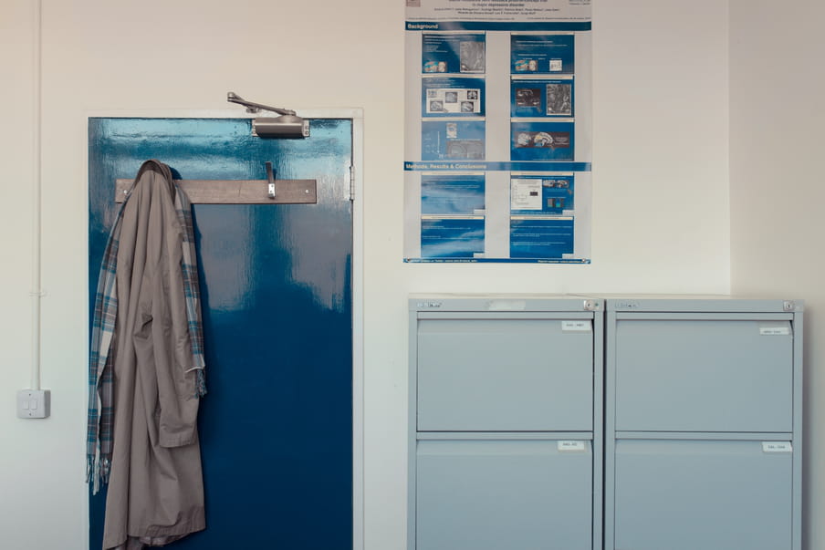 Office with two filing cabinets, a door with a coat hanging on it and a poster with brain graphics on the wall.