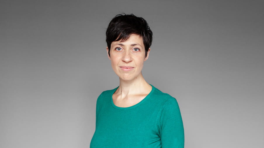 Photo of a woman in a green shirt - Irene Caselli - against a grey background.
