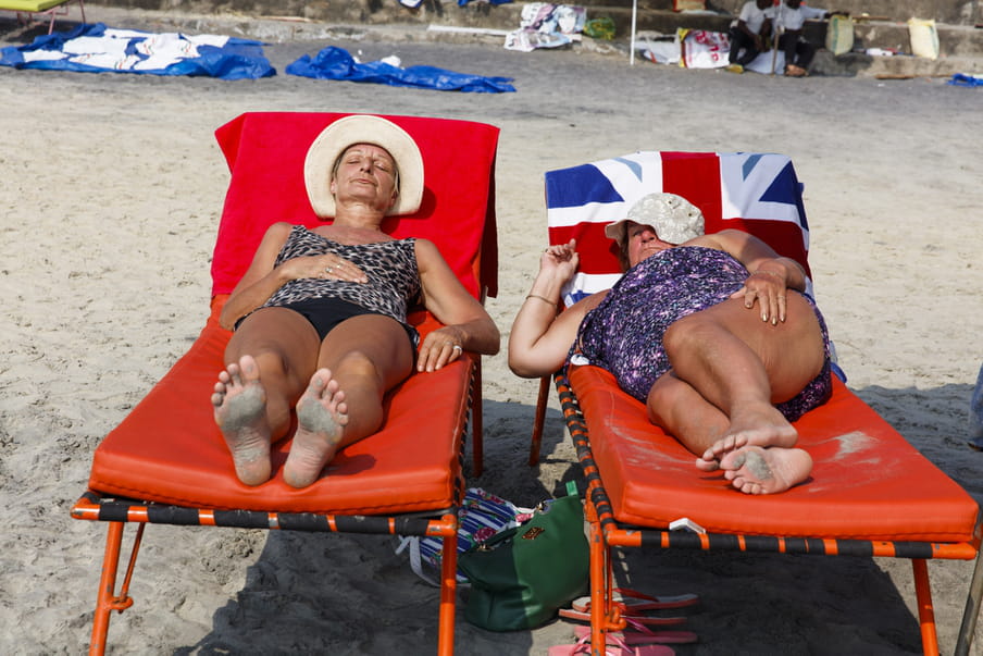 Photo of two women laying on beach beds, one with a towel with the UK flag on it