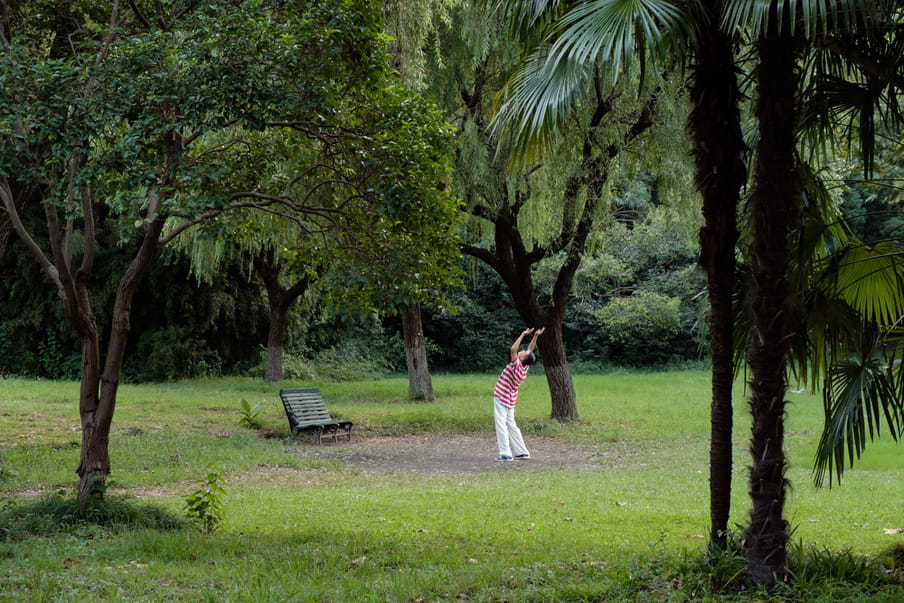 An old man stretching backwards in a green tropical park