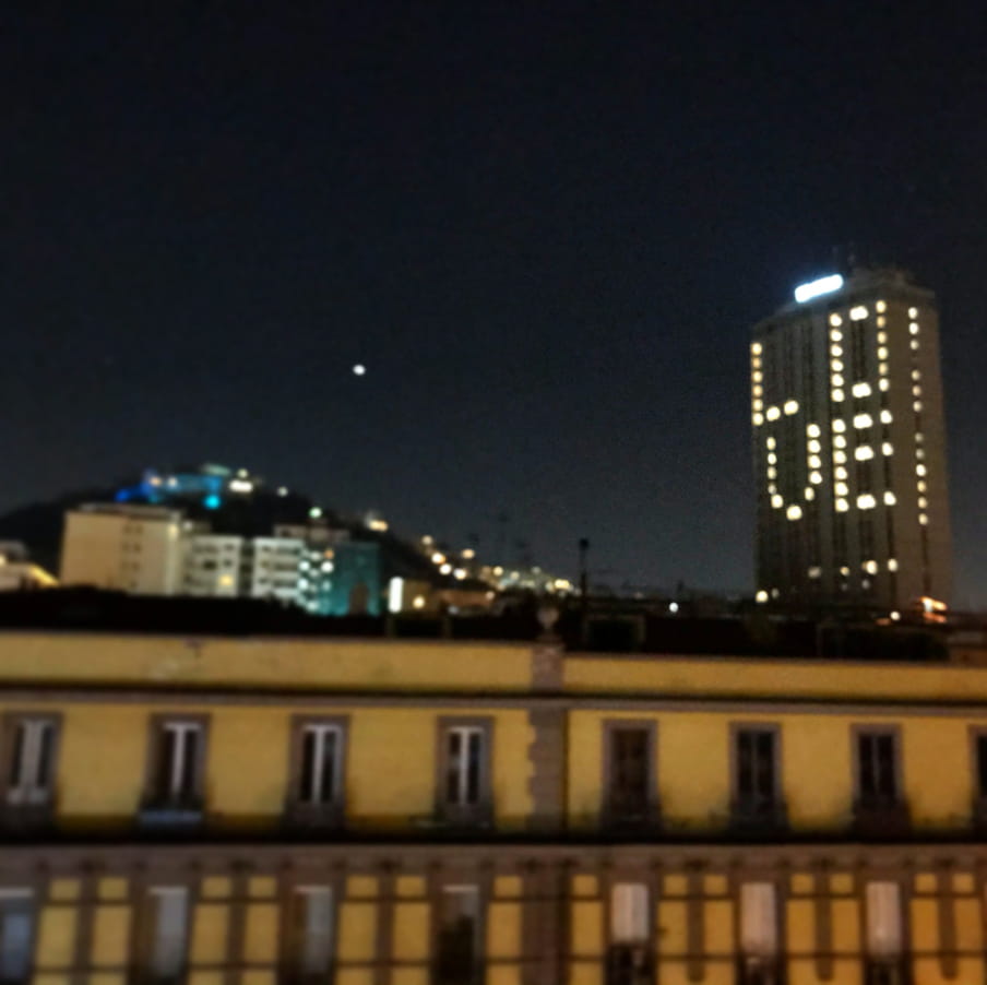 The view of a cityscape in Naples with a tall building lit with the word love spelled out thanks to lit windows.