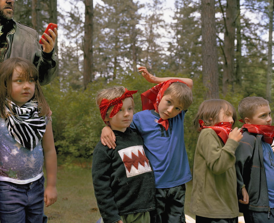 Photos of several kids standing in a row, with bandanas on their heads or arounds their necks. An adult in the back is checking his phone.