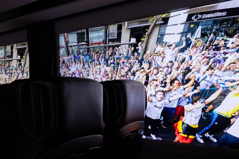 Photo from the inside of a coach. Outside fans of a football club are waving to the players. 