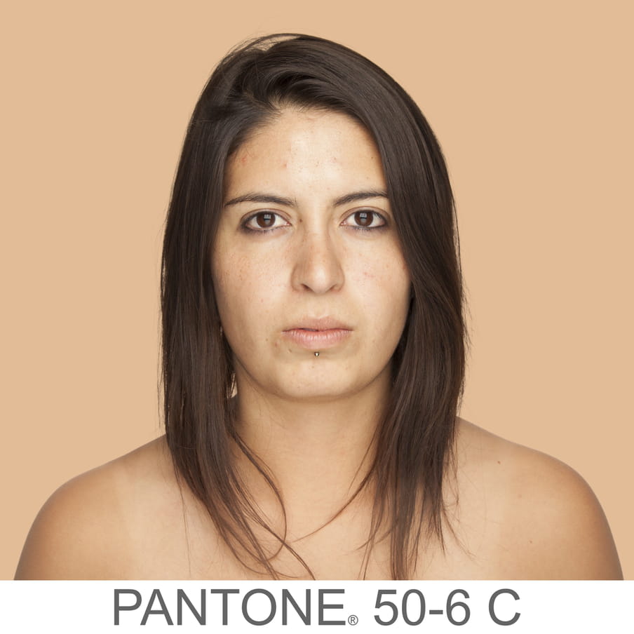 Photographic portrait of a woman brown middle long hair and a labret piercing. The background is a sample of 11 x 11 pixels taken from the nose of the subject and matched with the industrial pallet Pantone®. The pantone color is written out as PANTONE 50-6C. 