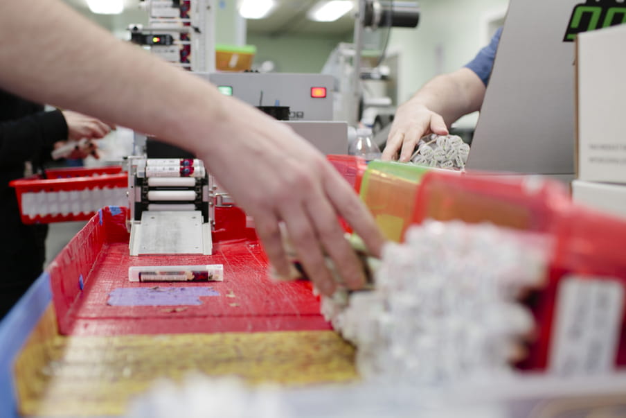 Photo with a close up of automated packaging machinery, several hands grabbing packages on top of it.