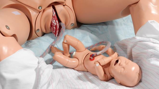 Photo of two dolls, one of a woman giving birth, umbilical cord still attached to a baby doll. 
